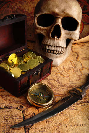 Pirate treasure. Old brass compass lying on a very old map with treasure chest full of golden coins, skull and knifeの写真素材
