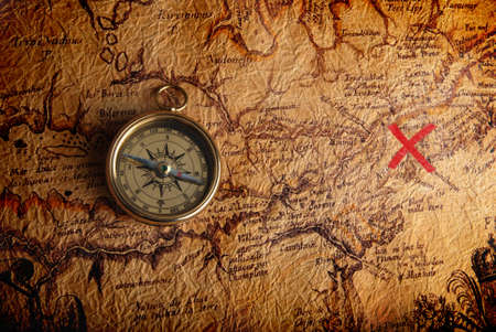 Old brass compass lying on a very old map showing the way to treasure