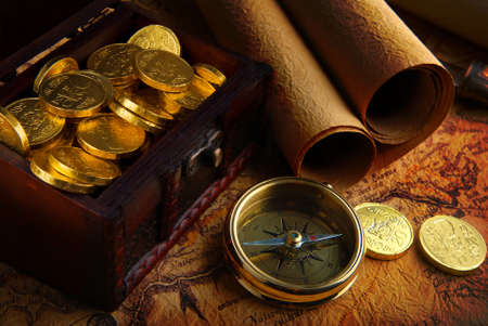 Old brass compass lying on a very old map with treasure chest full of golden coinsの写真素材