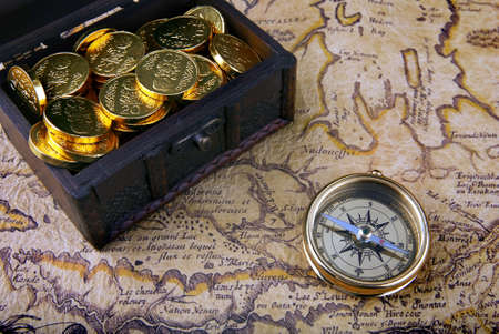 Old brass compass lying on a very old map with treasure chest full of golden coinsの写真素材