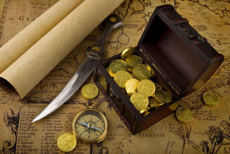 Old brass compass lying on a very old map with treasure chest full of golden coinsの写真素材