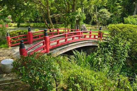 Beautiful Japanese garden with a lake and a red bridge in the frontの写真素材