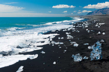 Beautiful beach in the South of Iceland with a black lava sand is full of icebergs from glaciers not far awayの写真素材