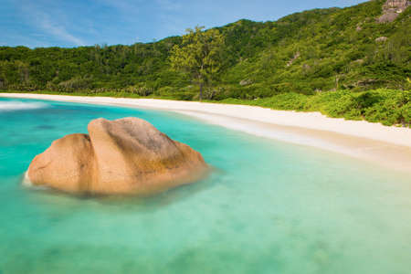 Beautifully shaped granite boulder in the turquoise sea (daytime long exposure technique) and a perfect white sand at Anse Coco, La Digue island, Seychellesの写真素材
