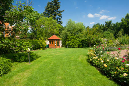 Beautiful garden with blooming roses, brick path and a small gazebo