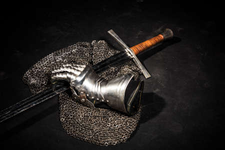 Medieval chain mail, iron gauntlet and a bastard sword still life on a dark backgroundの写真素材