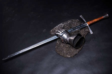 Medieval chain mail, iron gauntlet and a bastard sword still life on a dark backgroundの写真素材