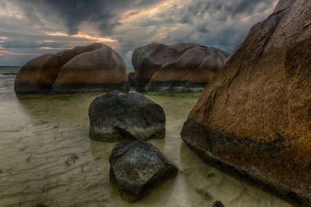 Beautifully shaped granite boulders in the sea of Seychelles at Anse Source d'Argent beach taken with a long exposure. Dramatic stormy sky at sunset timeの写真素材
