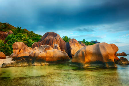 Beautifully shaped granite boulders in the sea of Seychelles at Anse Source d'Argent beach taken with a long exposure. Dramatic stormy sky at sunset timeの写真素材