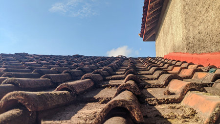 A close-up view of a tiled roof. The tiles are brown and arranged in rows. The roof is sloping...