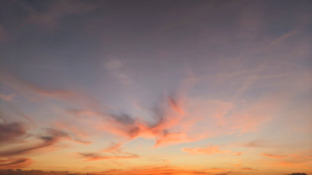 A beautiful sunrise sky with shades of orange, pink, and purple. The clouds are dramatic and form interesting patterns. The horizon is barely visible, blending into the sky.の写真素材