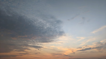 A dramatic sky with shades of gray, orange, and pink. The clouds are thick and appear to be moving quickly. The sky is divided into two distinct sections: gray area and a lighter, pink and orange areaの写真素材