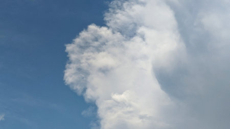 A towering cumulus cloud dominates the sky, its fluffy, white form contrasting against the deep blue backdrop. The image evokes a sense of wonder and the vastness of nature.の写真素材