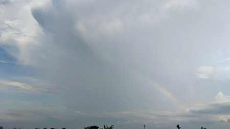 A partial rainbow arches across a cloudy sky. The vibrant colors of the rainbow stand out against...