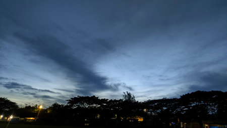 A dramatic sunrise sky with a mix of dark, stormy clouds and a vibrant orange sunrise. The clouds create a sense of depth and movement, while the warm hues of the sunrise provide a striking contrast.の写真素材
