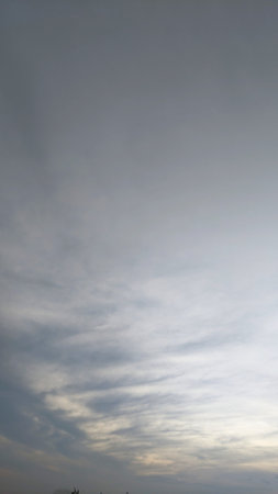 The image showcases a dramatic sky blanketed by a thick layer of dark, swirling clouds. Hints of a vibrant sunrise peek through, casting a warm glow on the lower horizon.の写真素材