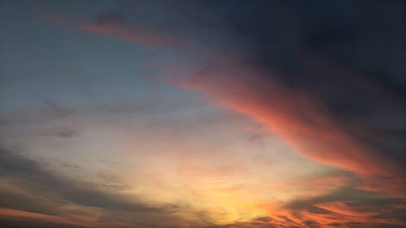 Dramatic sky with dark storm clouds contrasting with a vibrant, fiery sunrise glow at the horizon....