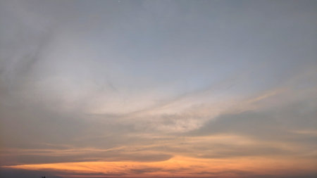 A dramatic sky at sunset or sunrise, displaying a gradient of light orange, pink, and blue, with sweeping cloud formations and a faint star.の写真素材