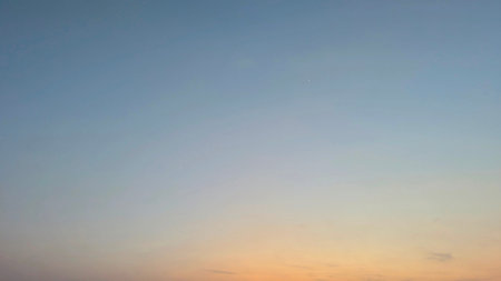 A serene sunrise sky with a subtle gradient from soft blue to warm orange at the horizon, featuring...