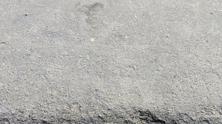 A detailed close-up of rough, grey asphalt or concrete, showcasing its coarse texture and granular surface under natural light.の写真素材