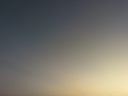 A serene sky with a smooth gradient from deep grey-blue at the top to a gentle, warm yellow-orange...