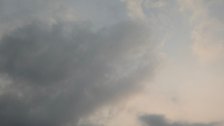 A vertical view of a cloudy sky with soft, diffused light. The thick gray and white clouds, with a...