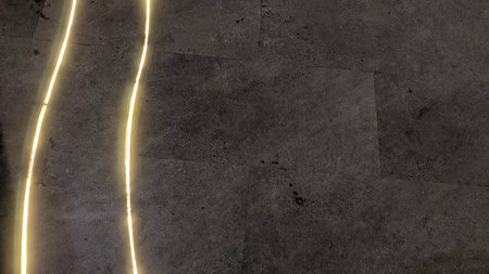 A dark gray textured ground surface with a diagonal yellow strip of light. The light appears to be...