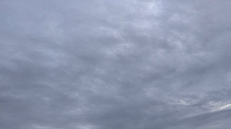 A gray, cloudy sky with a soft, uniform texture. The clouds are layered and form a dense covering,...