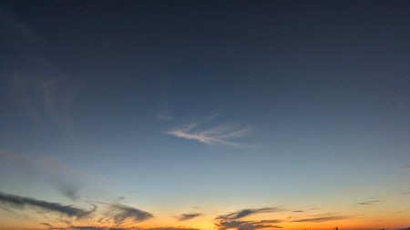 A serene sunrise sky with a deep blue-to-orange gradient and wispy clouds near the horizon. Two bright dots, possibly stars or planets, are visible in the upper part of the frame.の写真素材