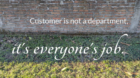 A brick wall and grass are visible in the background while the text &quot;Customer is not a department, it&#39;s everyone&#39;s job&quot; is written in the foreground in a stylish font.の写真素材