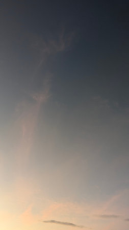 A soft gradient of color fills a quiet evening sky. The top is a deep, dusky blue that smoothly transitions into a pale peach and hints of orange at the bottom.の写真素材