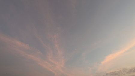 A peaceful sky at dawn with a gradient of soft, muted colors. . The sky transitions from a pale gray-blue at the top to a gentle pink and orange at the bottom. Wispy clouds add texture to the scene.の写真素材