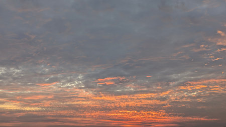 A beautiful and dramatic sunrise sky with a wide expanse of clouds. The upper part is a soft gray,...