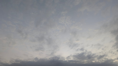 A cloudy dawn sky with a soft light source just below the horizon, creating a gentle gradient from light to dark. The clouds are varied, some wispy and high, others heavier and low.の写真素材