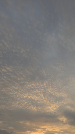 A vertical image of a cloudy sky at sunrise, with a pattern of small, textured clouds.の写真素材