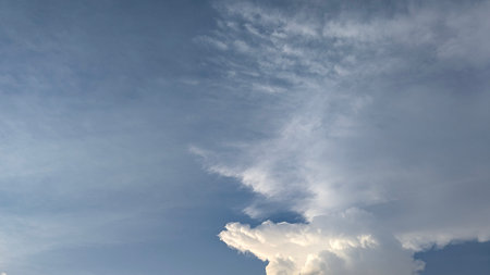 A dynamic sky scene featuring a large, textured white cumulonimbus cloud on the right, contrasted...