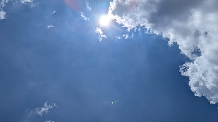 The bright sun bursts through dramatic white clouds, illuminating a deep blue sky. A natural frame is created by the clouds, leaving ample copy space below. Dramatic sky abstract.の写真素材