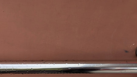 A smooth reddish-brown painted wall with a wet chrome handrail running horizontally across the...