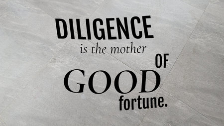 Diligence is the mother of good fortune. This inspiring quote is displayed in bold, black text on a sleek gray tile floor, offering motivation for hard work.の写真素材