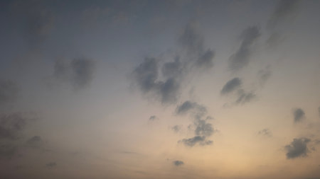 A subtle, serene dawn sky shows soft, scattered clouds against a gradient of muted blue gray to warm peach yellow, suggesting peace tranquility.の写真素材