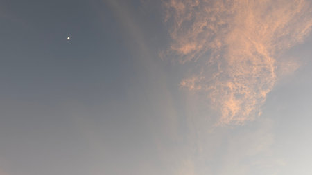 A peaceful dawn sky with a visible crescent moon and a patch of cirrus clouds illuminated by the...