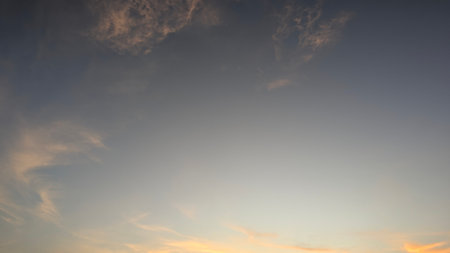 A subtle, tranquil dawn sky with a smooth gradient from deep gray-blue to warm gold and soft pink clouds near the horizon, suggesting an early morning scene.の写真素材