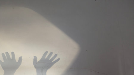 Abstract image of two dark shadows of hands reaching out onto a textured wall, with a bright spotlight effect creating high contrast and ample gray copy space for text or design elementsの写真素材