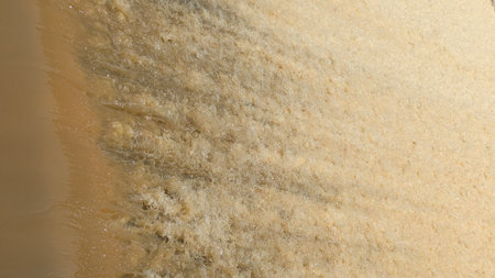 Abstract of fast-flowing, yellowish-brown water foaming and frothing as it rushes over an unseen...