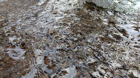 Long exposure close-up of clear water flowing over smooth river stones, pebbles, creating abstract,...