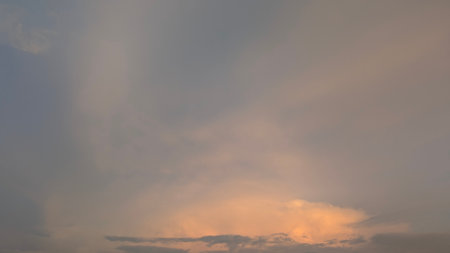 Soft, diffuse clouds fill the expansive sky, colored in grayish-blue, peach, orange hues. This scene...