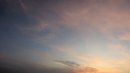 A vast dawn sky features soft, wispy clouds in muted pink, orange, blue tones. Gentle light creates a serene, atmospheric background, perfect for nature, calm, peaceful themes.の写真素材
