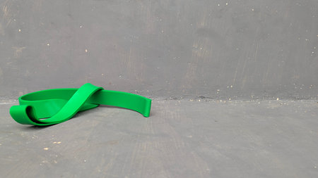 A green resistance band lies uncoiled on a textured grey concrete floor. This minimalist fitness scene features industrial elements, a simple color palette. It provides a versatile background for sports, wellness, home workout content, commercial design. The composition highlights tools for strength, physical health.の写真素材