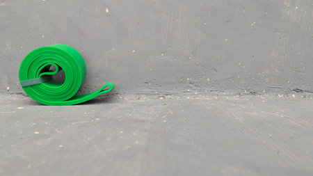 A rolled green resistance band rests against a textured grey concrete wall. This minimalist fitness scene features a high-angle view with industrial elements, simple color palette. It provides a versatile background for sports, wellness, home workout content, commercial design. The composition highlights tools for strength, physical health.の写真素材