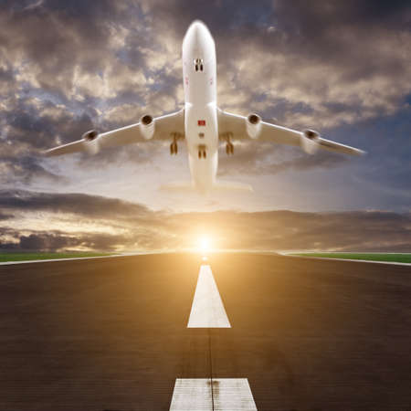 passenger plane fly up over runway from airport at sunsetの写真素材